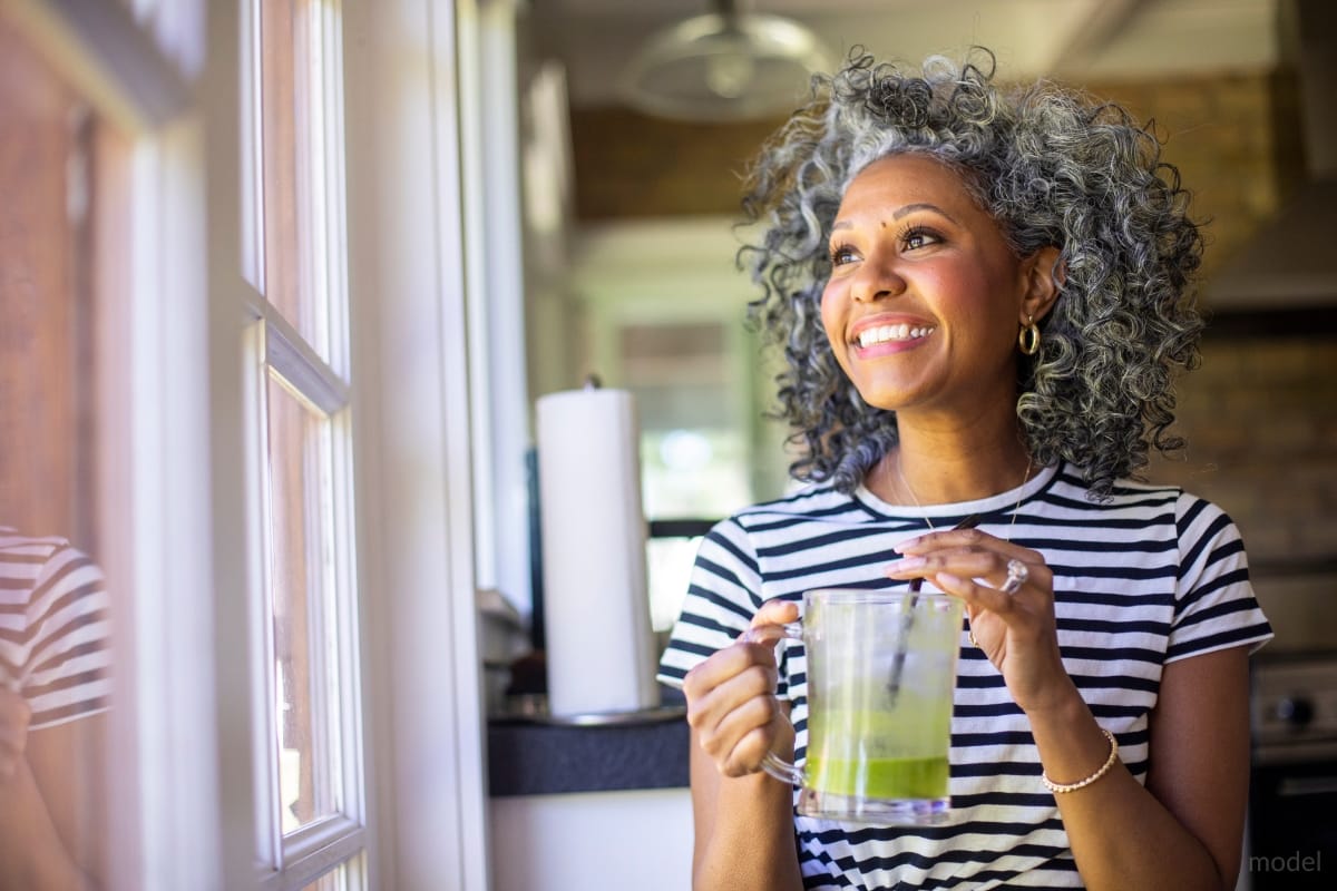 Middle-aged woman smiling with a cup of green juice